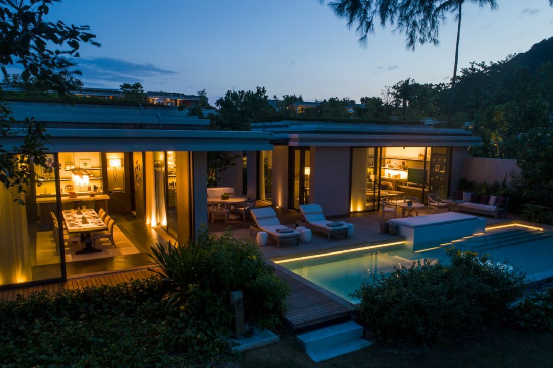 The front view of a private Phuket villa with a pool, dining room, kitchen, and living room with soft lights