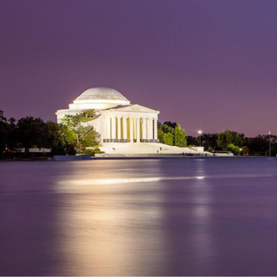 The Jefferson Memorial illuminated at night, reflected in the calm waters of the Tidal Basin.