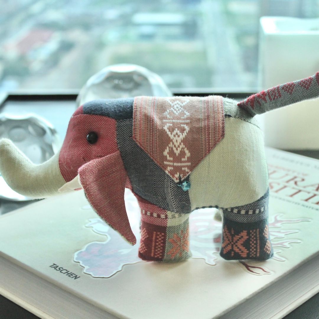A fabric elephant toy with a patchwork design, placed on a book.