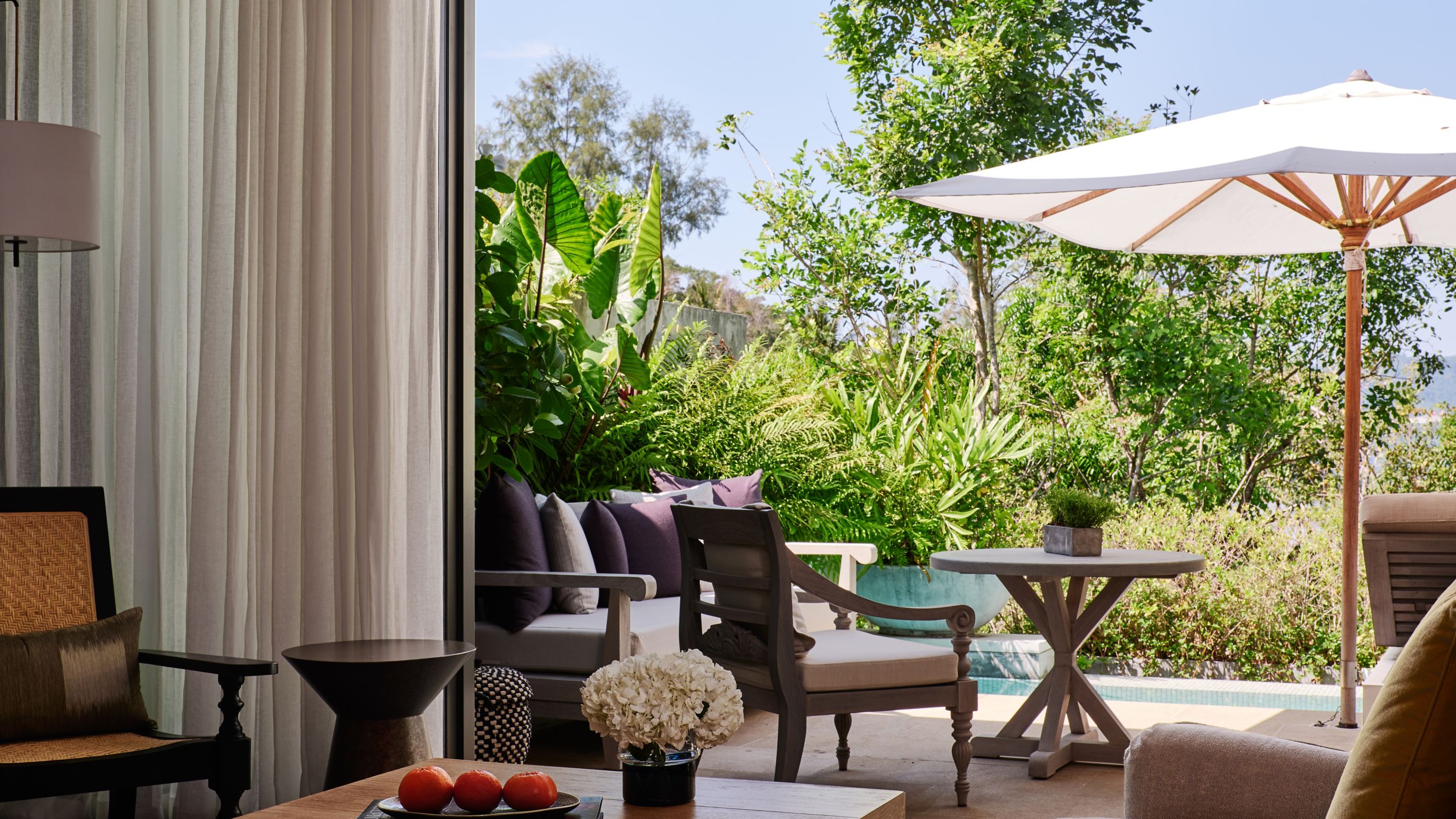 An outdoor lounge with seating, surrounded by greenery, a private plunge pool, and a table
