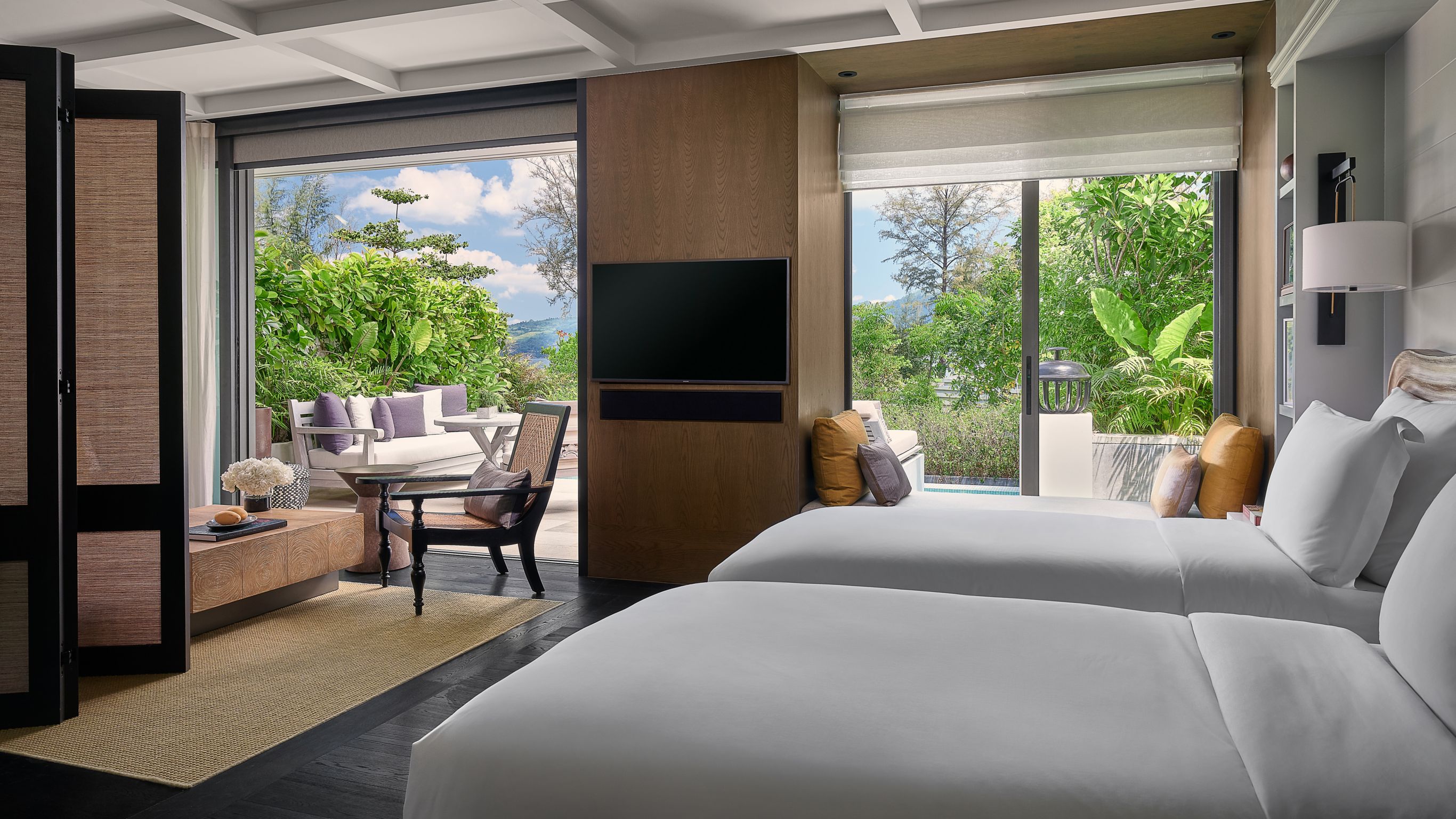 Garden Pool Pavilion Bedroom Phuket - Resort room with two beds, a wall-mounted TV, and large windows opening to an outdoor patio with seating and greenery.