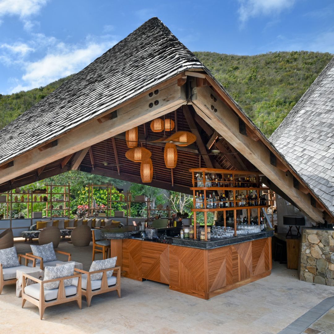 A wine and rum bar beneath a wooden, triangle-shaped pergola featuring cozy lounge chairs.