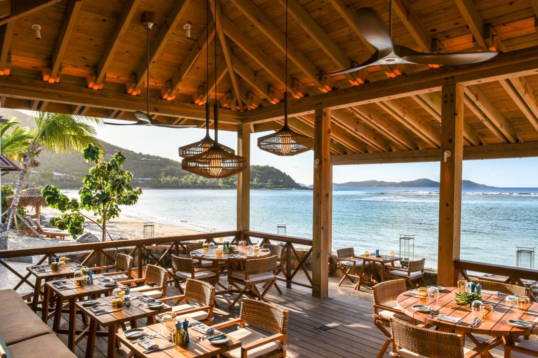 A beachfront restaurant with ocean views, where dining tables sit elegantly beneath a wooden roof.
