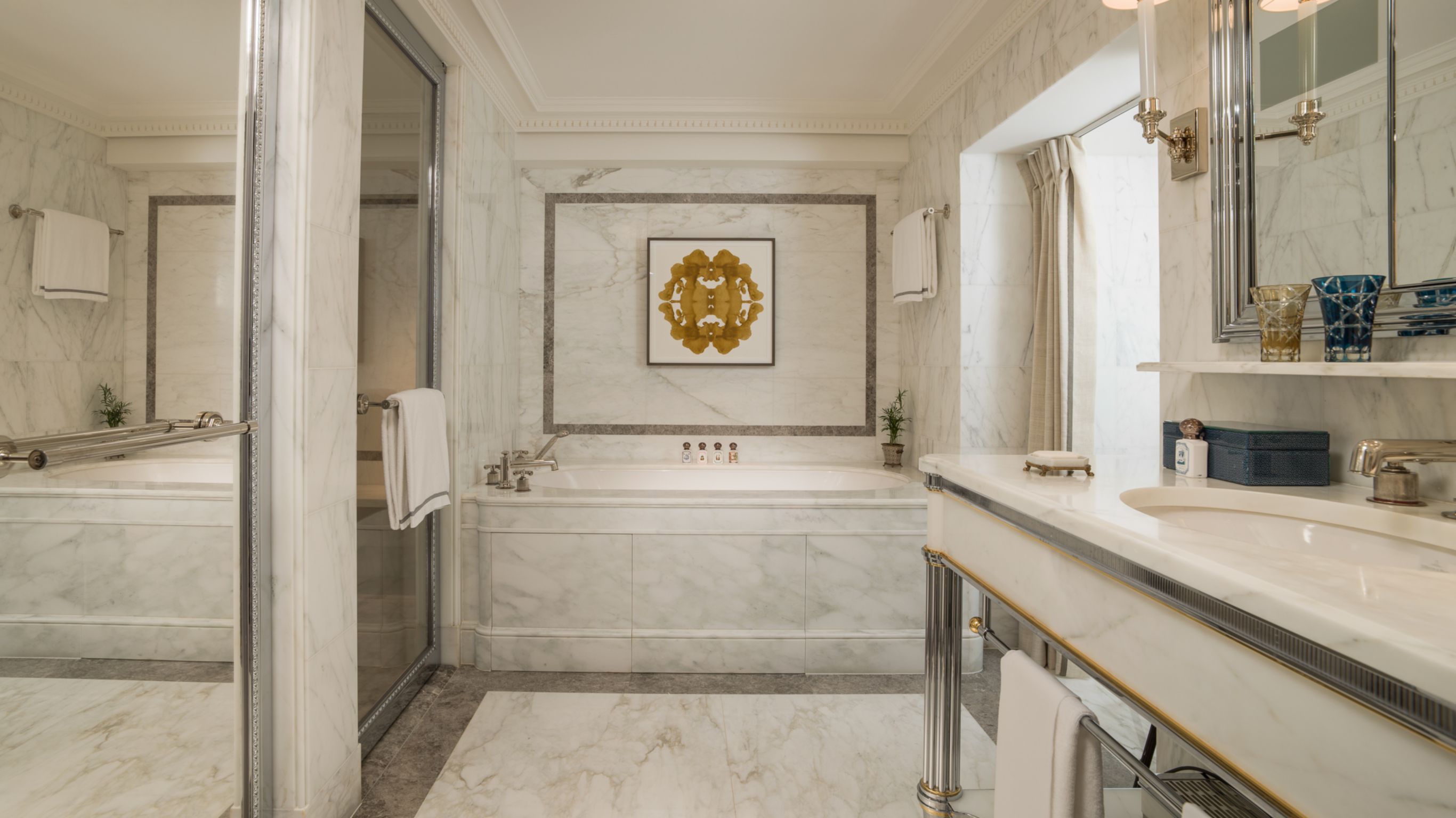 A luxurious marble bathroom featuring a deep soaking tub, framed by gray and gold accents, and a large mirror.