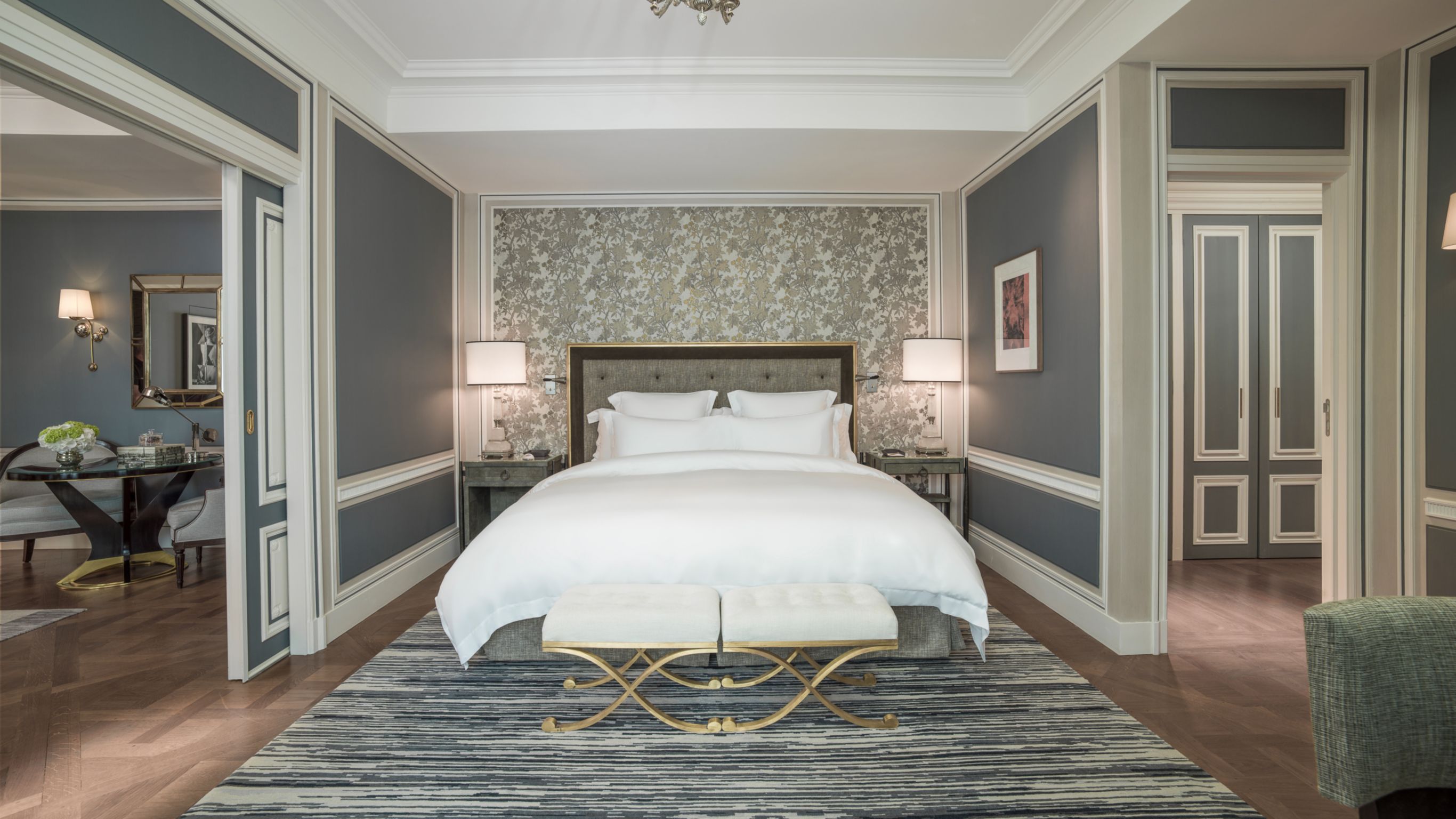 Luxurious hotel suite with a large bed in the center and gray wall dividing the hotel room.
