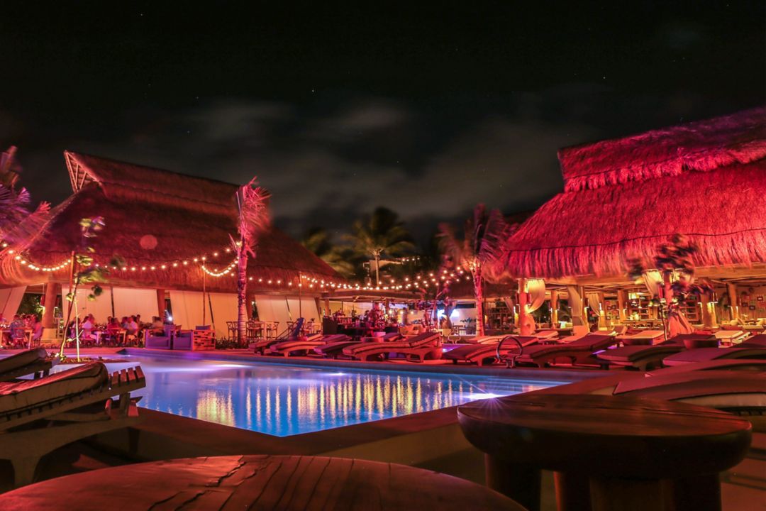  La gente se sienta en mesas largas en la arena bajo luces de cuerda por la noche