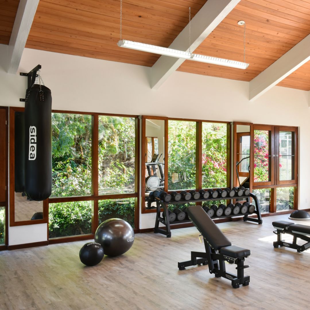 Bright fitness center with weights, benches, a punching bag, and large windows.
