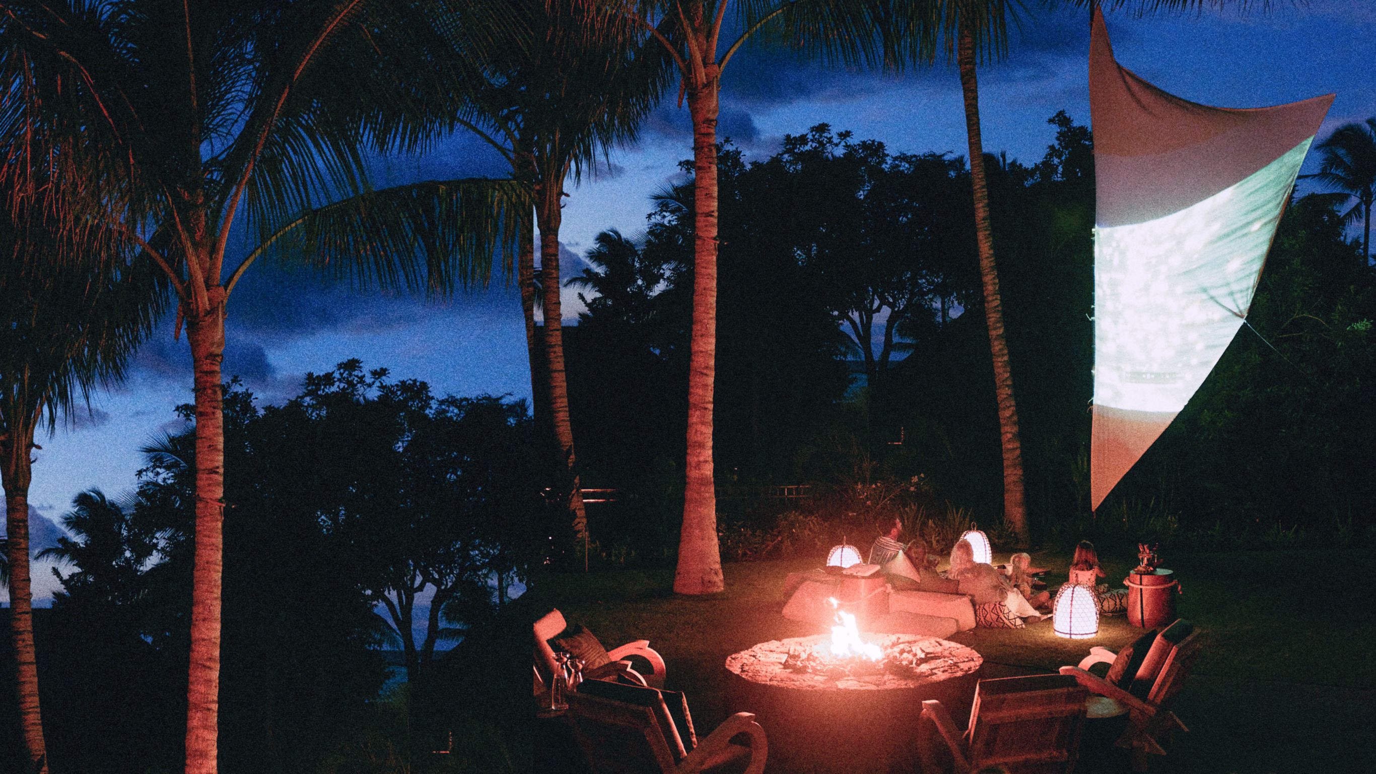 A group of people sitting around a fire in a tropical setting at night in Kona, Hawaii.