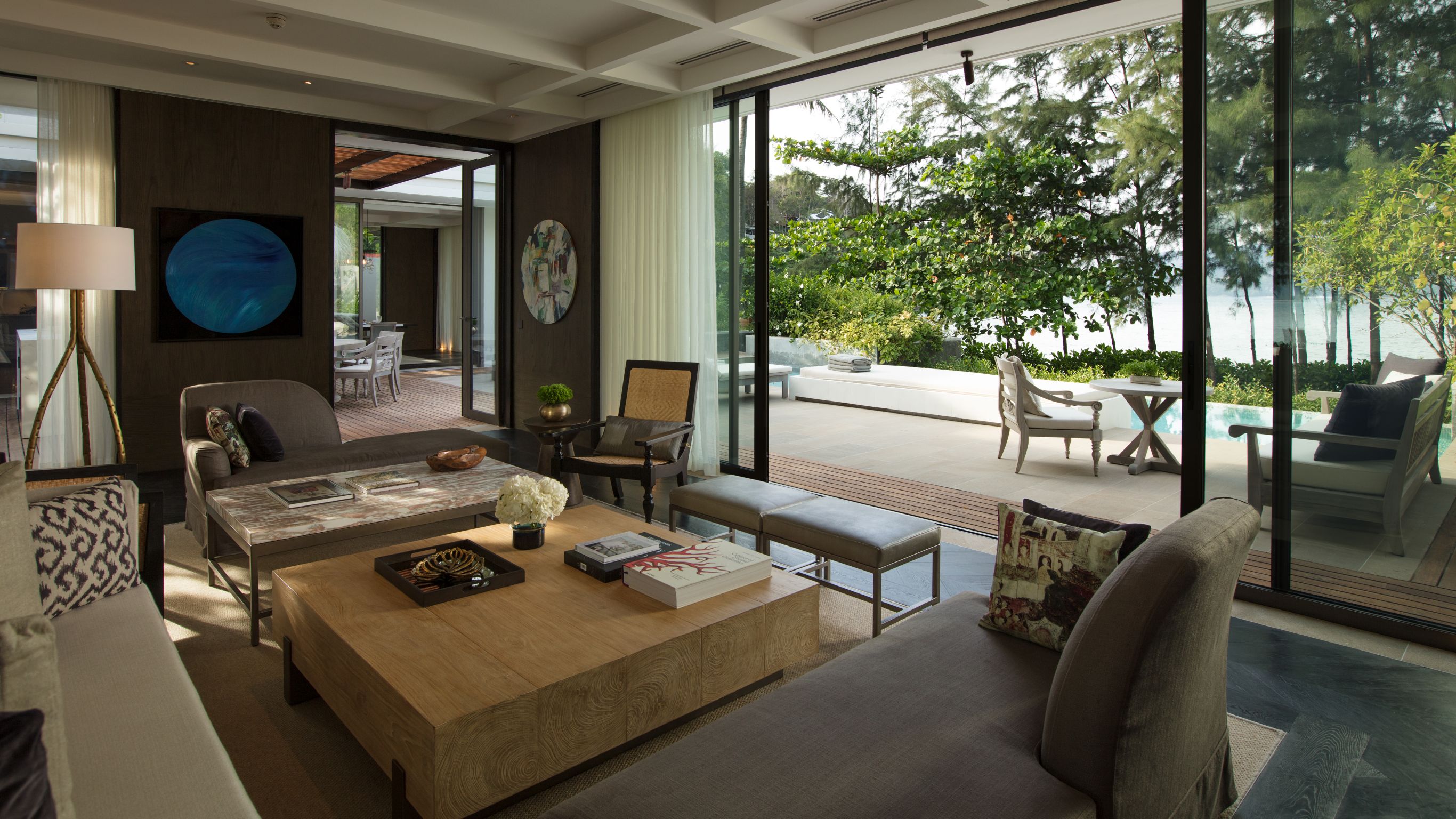 Phuket luxury villa - A hotel suite lounge area with a gray sofa and a centerpiece overlooking the backyard with a view of the sea