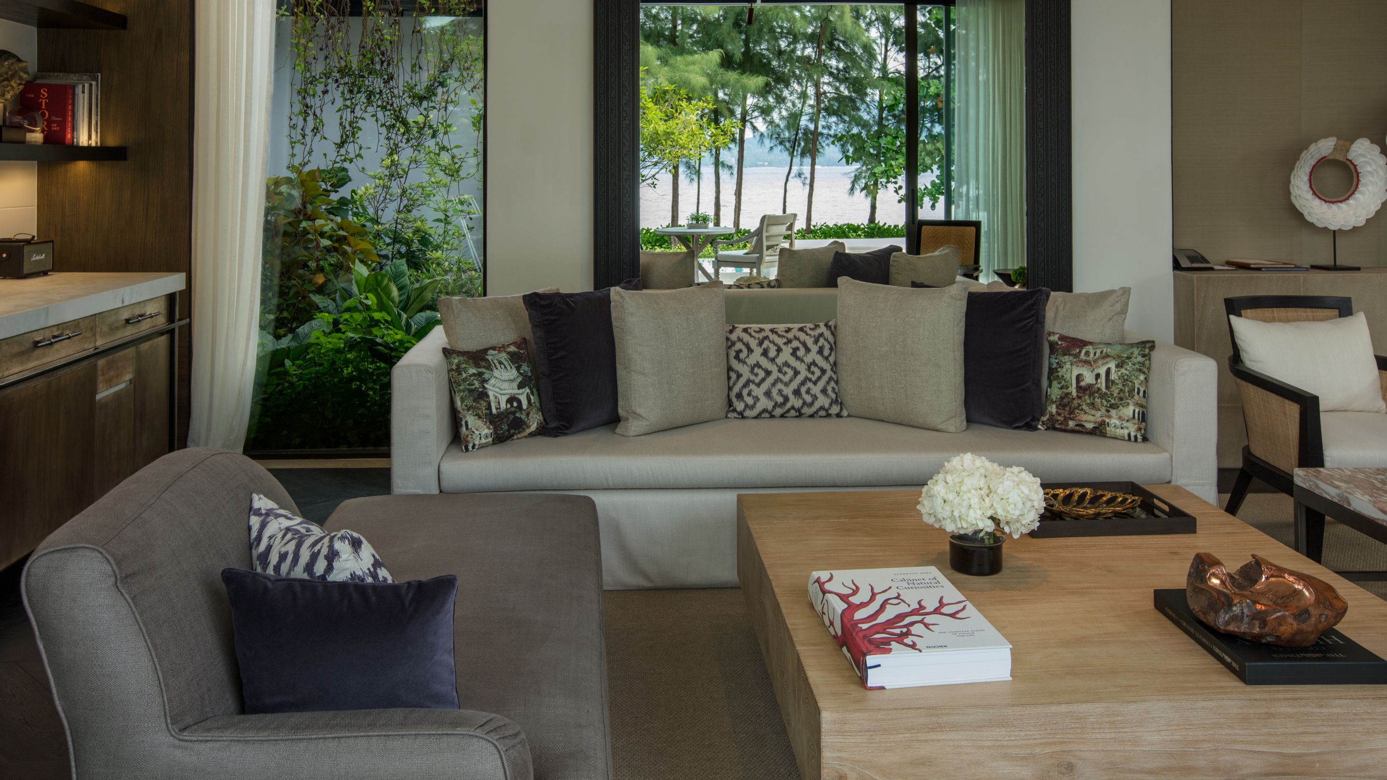 Phuket luxury villa - The lounge area in a private villa with sofas, a large wooden table, and windows showing trees outside.