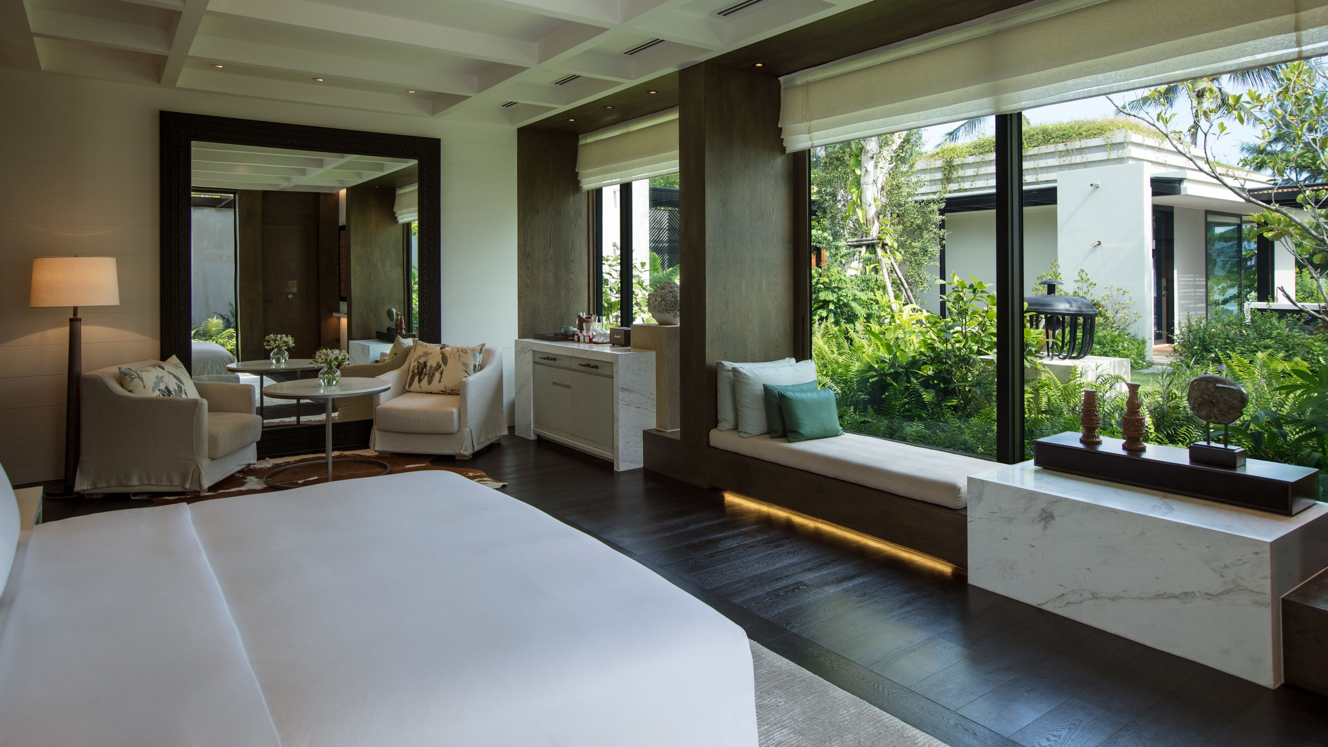 Large hotel room with bed, small table and armchairs near a large mirror.