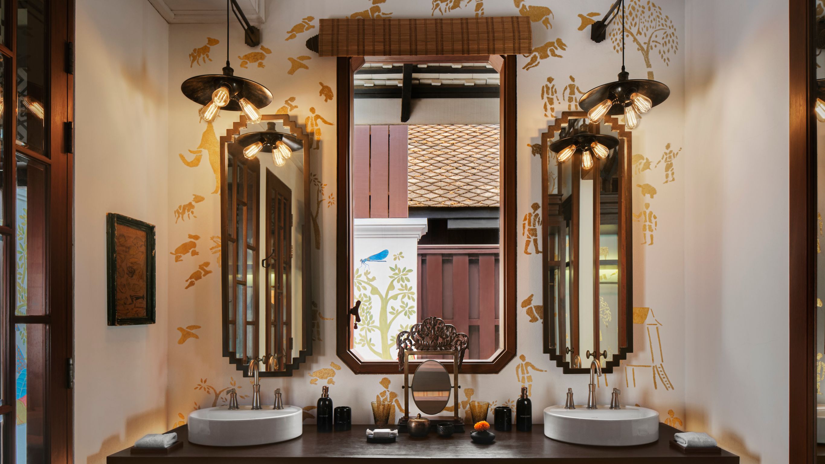 A luxury hotel bathroom designed by Bill Bensley featuring a double vanity and three vertical mirrors in Luang Prabang