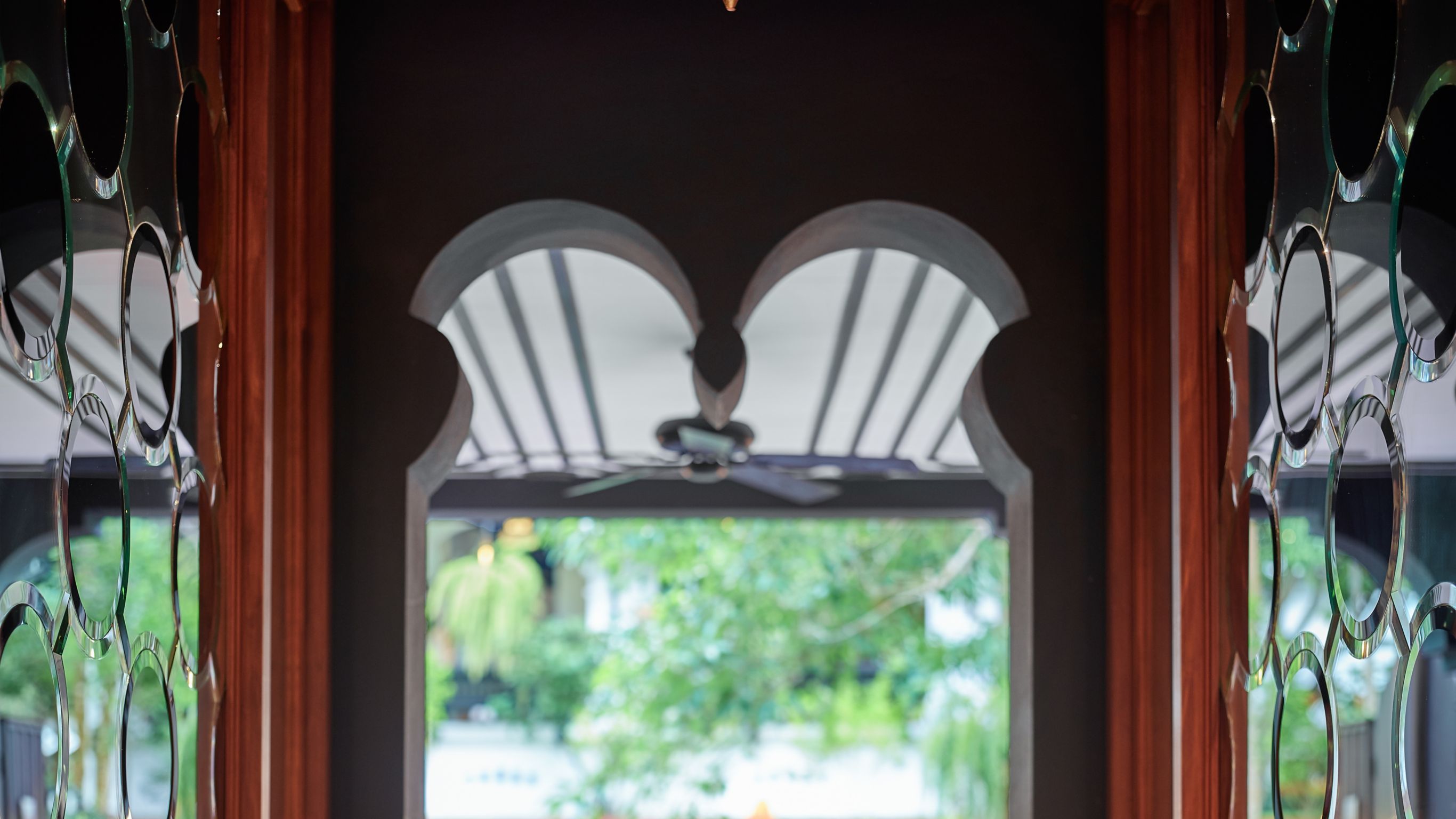 View through glass doors of an outdoor seating area with orange pillows surrounded by greenery.