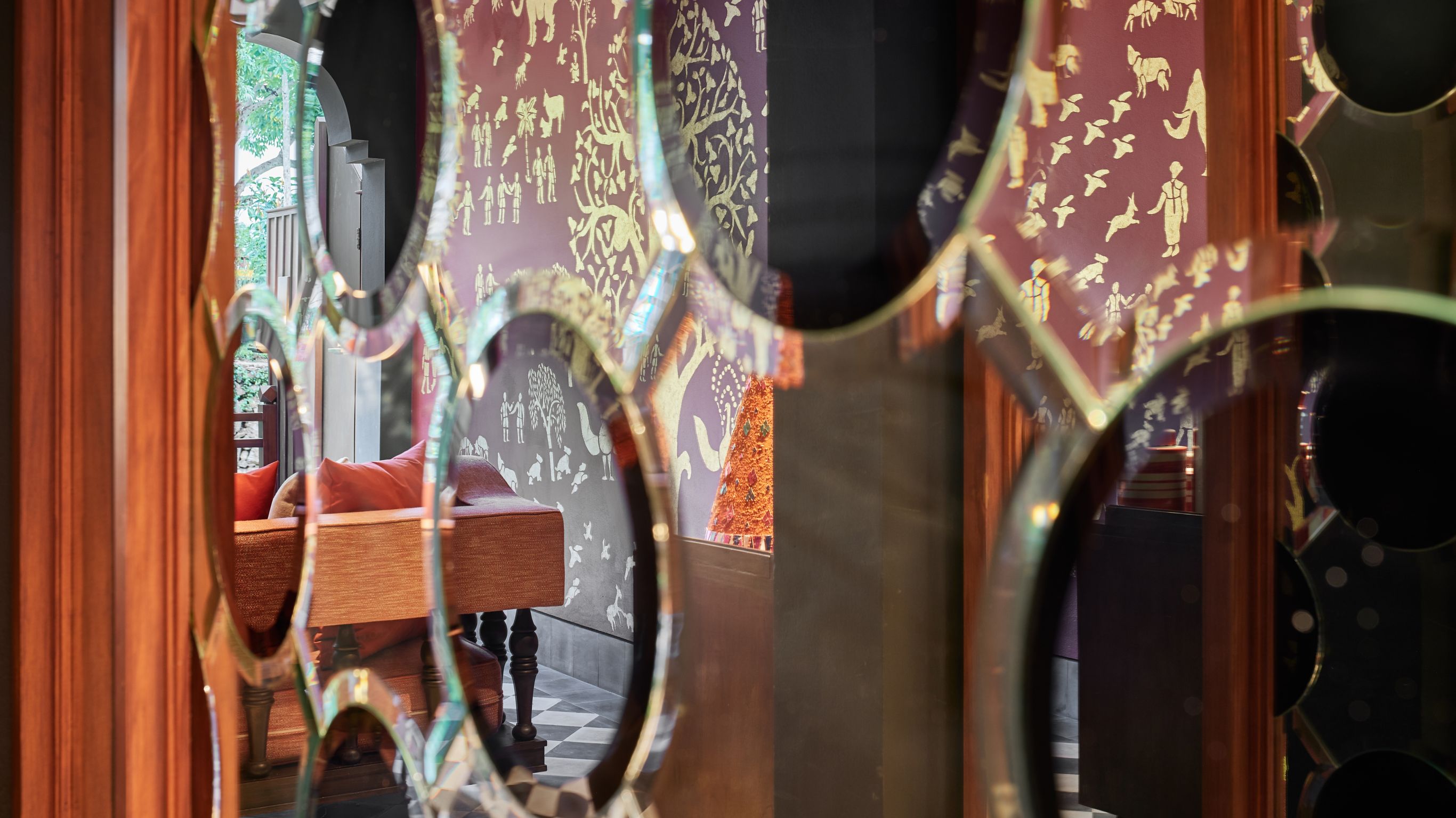 Glass doors with decorative patterns, leading to a room with patterned walls, a wooden table, and cushions.