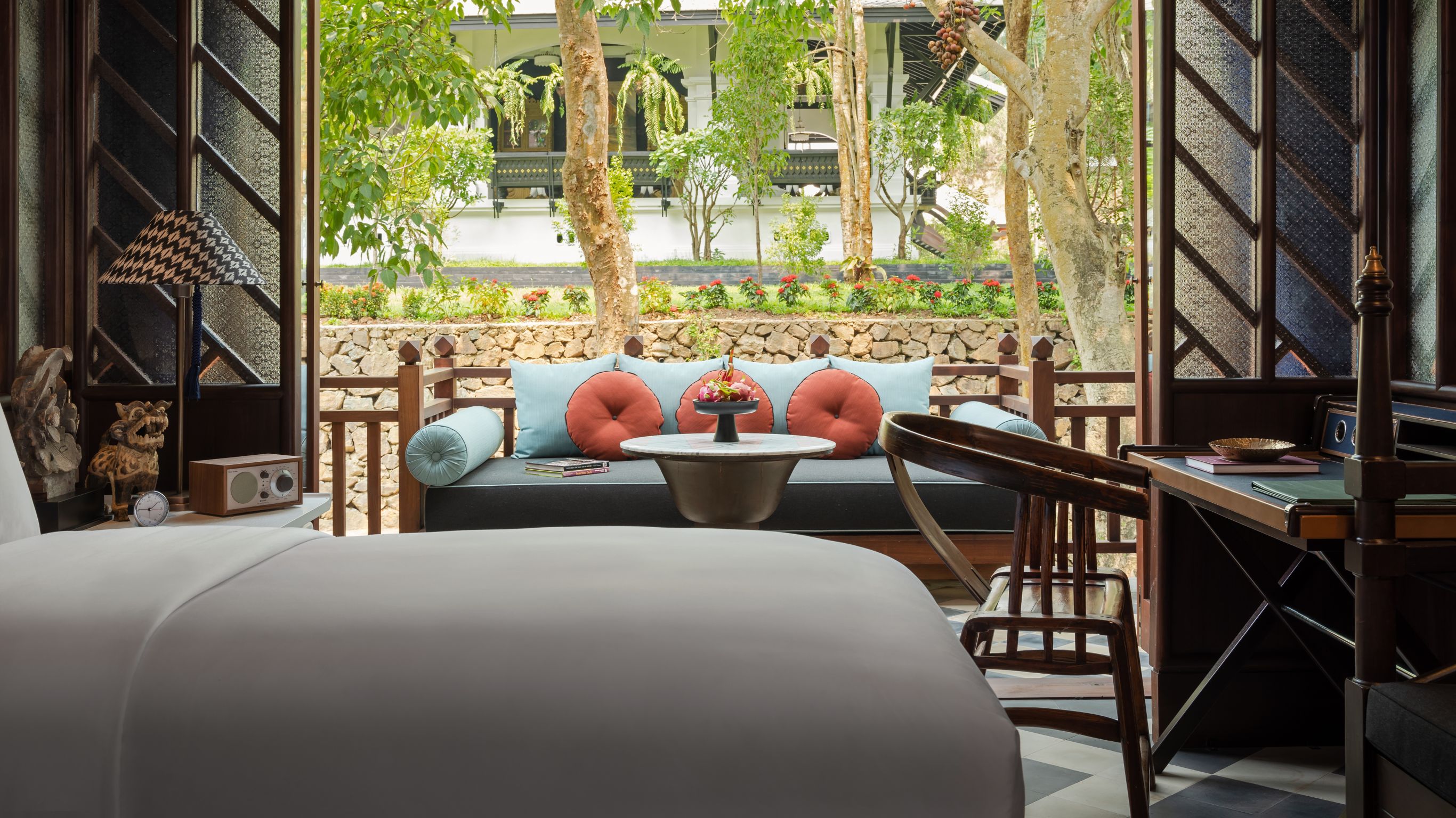 A luxury hotel room designed by Bill Bensley with bed, outdoor seating area, and garden view., in Luang Prabang
