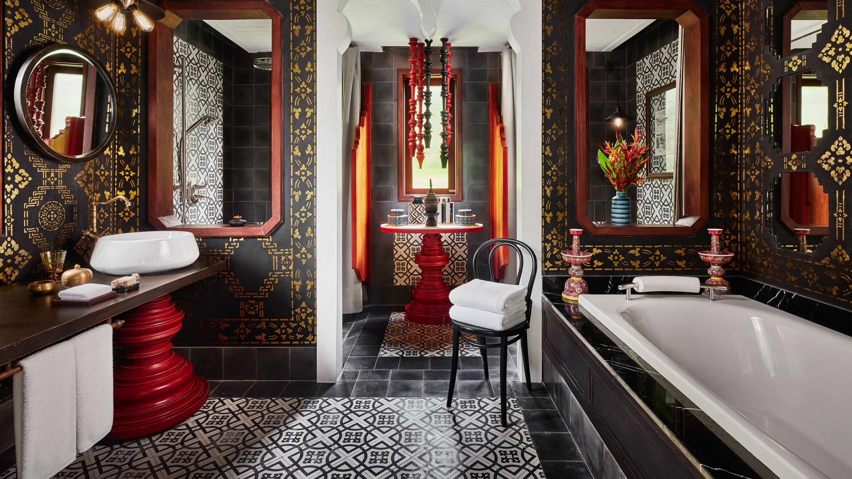 Bill Bensley designed hotel bathroom in Luang Prabang with black and gold tiles, red accents, bathtub, mirrors, and decorative elements.