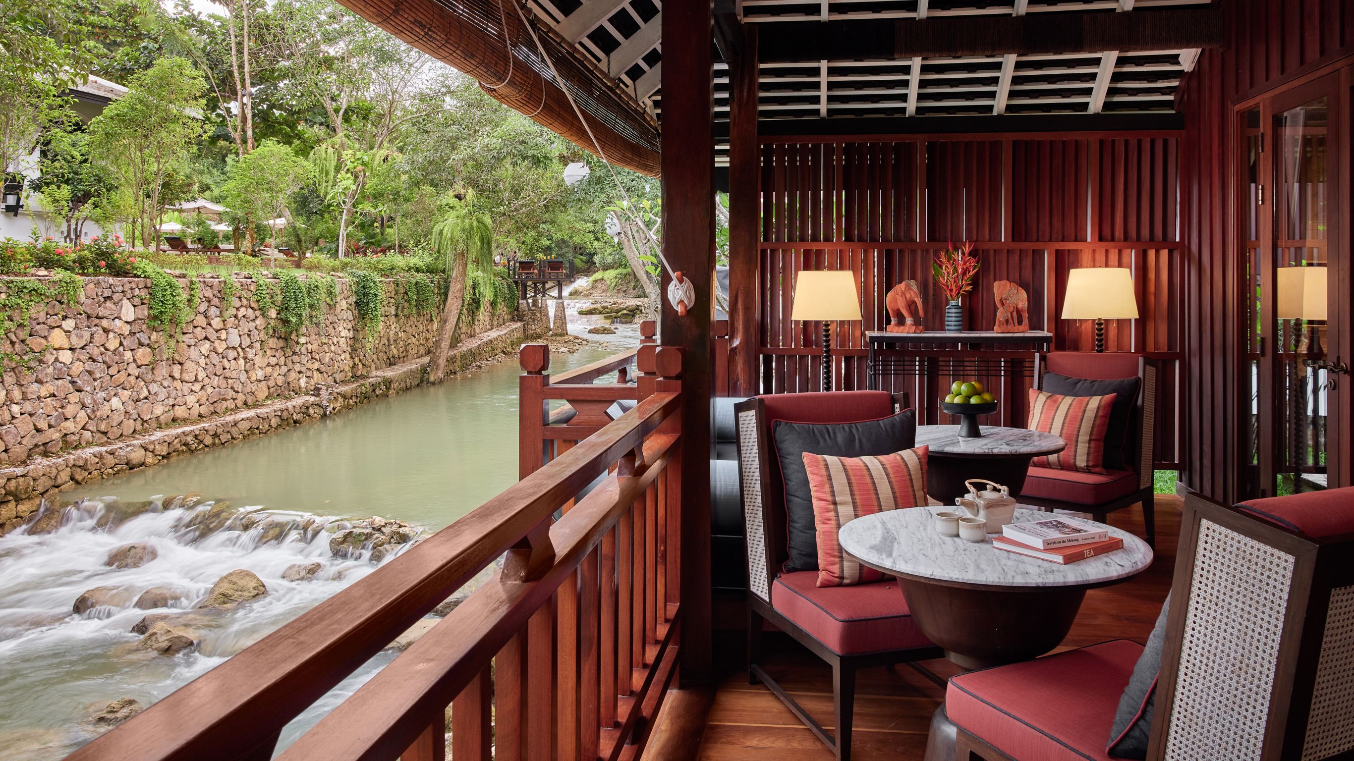A balcony with red lounge chairs overlooking a river in Luang Prabang