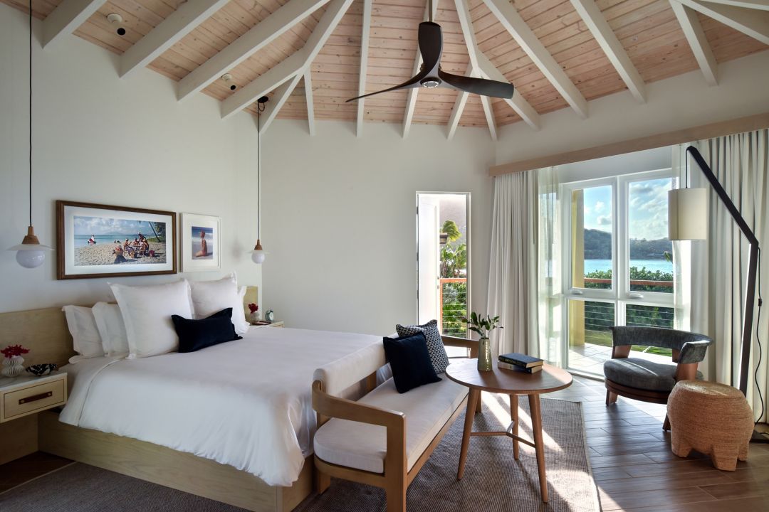 Modern bedroom with a king-size bed, wooden furniture, and a balcony overlooking a beach view.