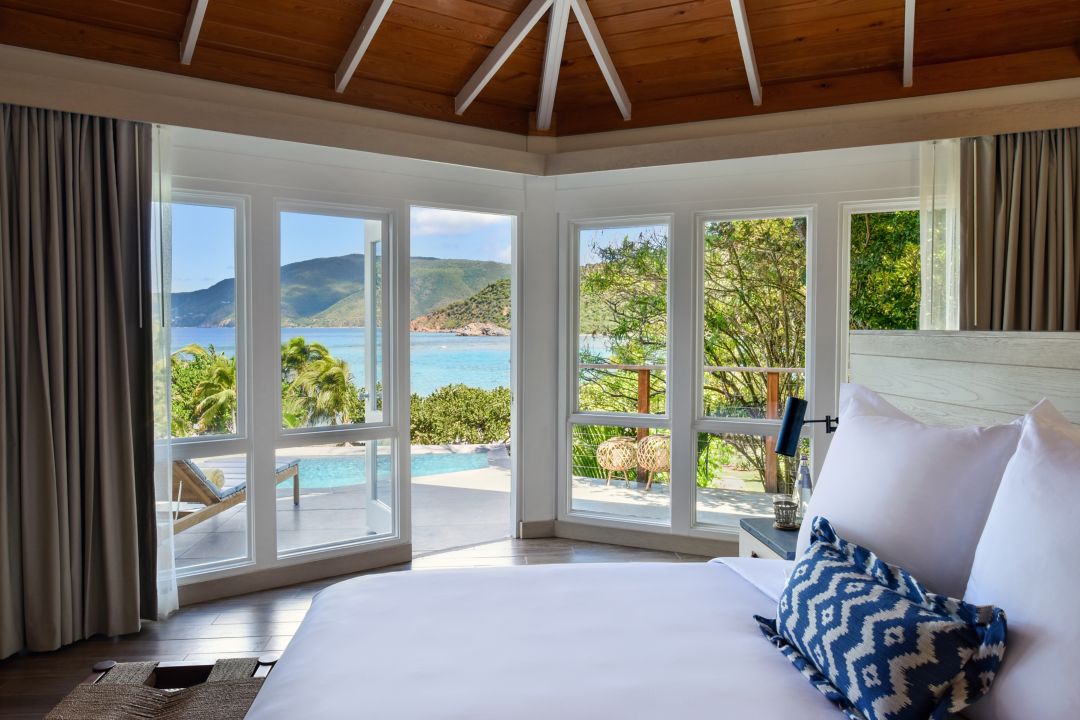 Bright hotel suite bedroom with large windows overlooking a private pool and ocean view.