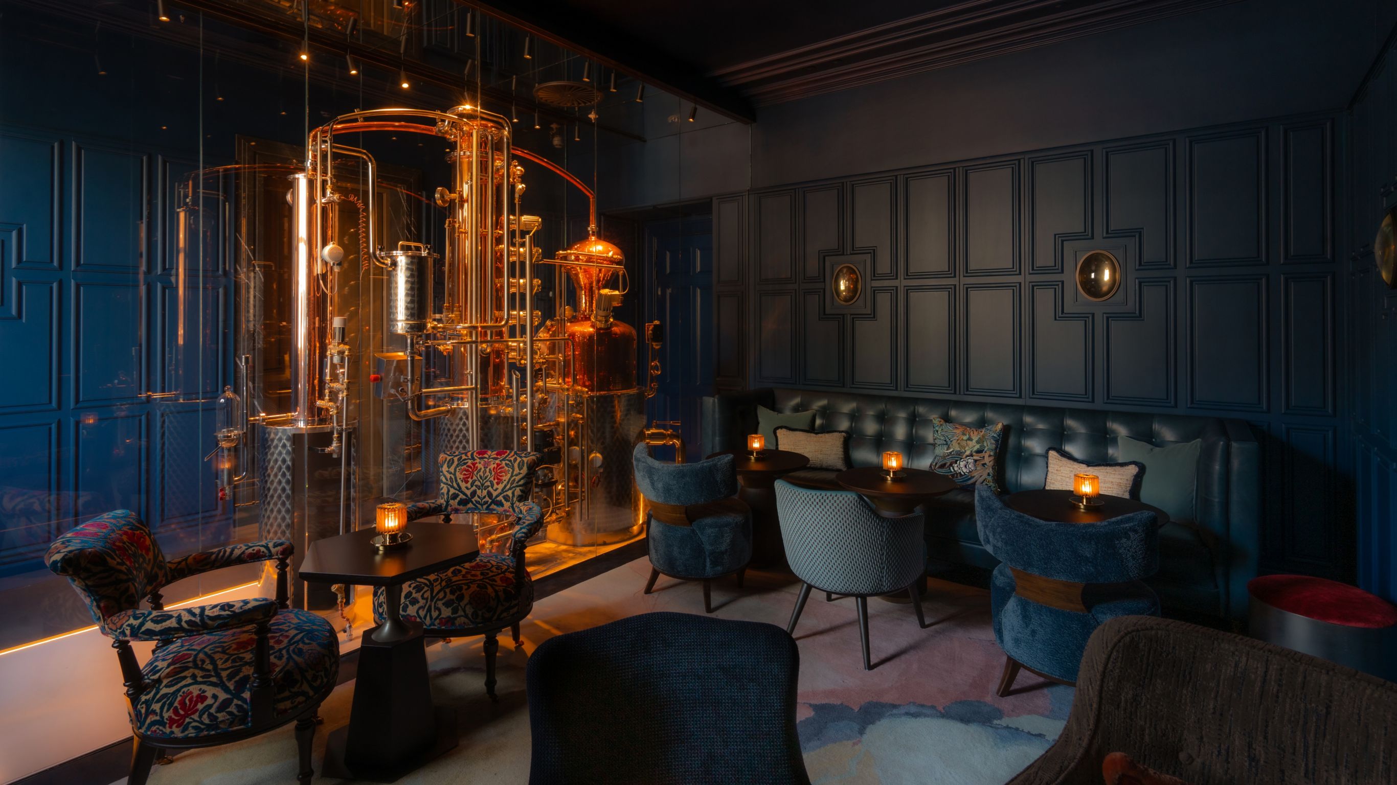 Lounge bar with dark walls, copper distillery,  and plush seating with candles.