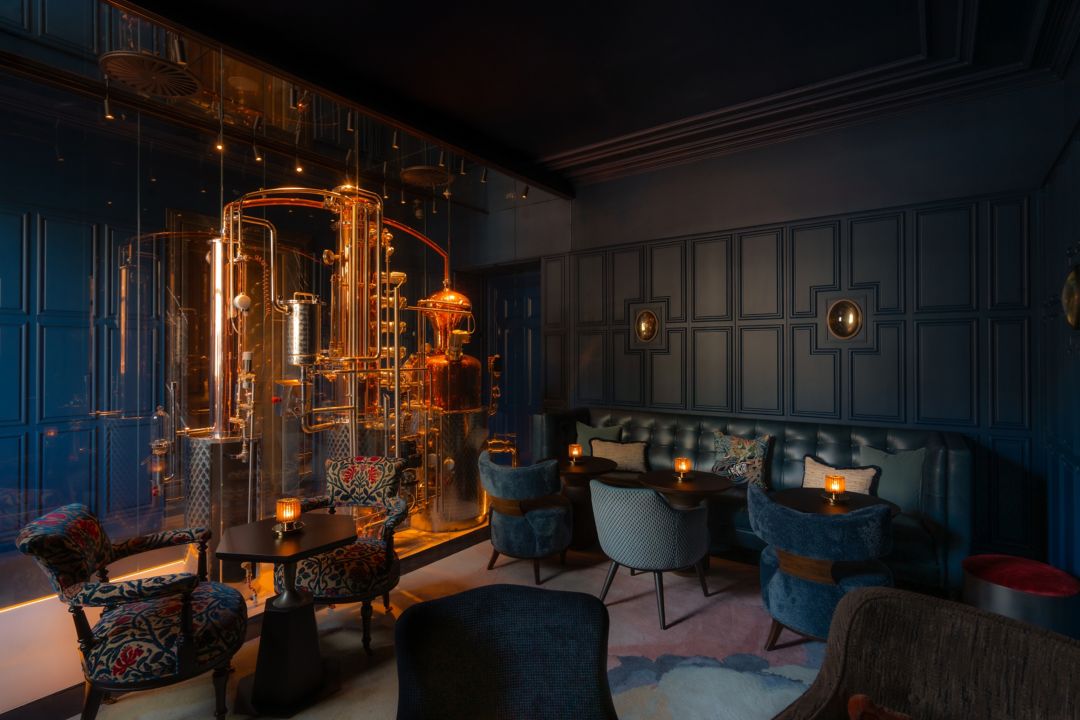 Lounge bar with dark walls, copper distillery,  and plush seating with candles.