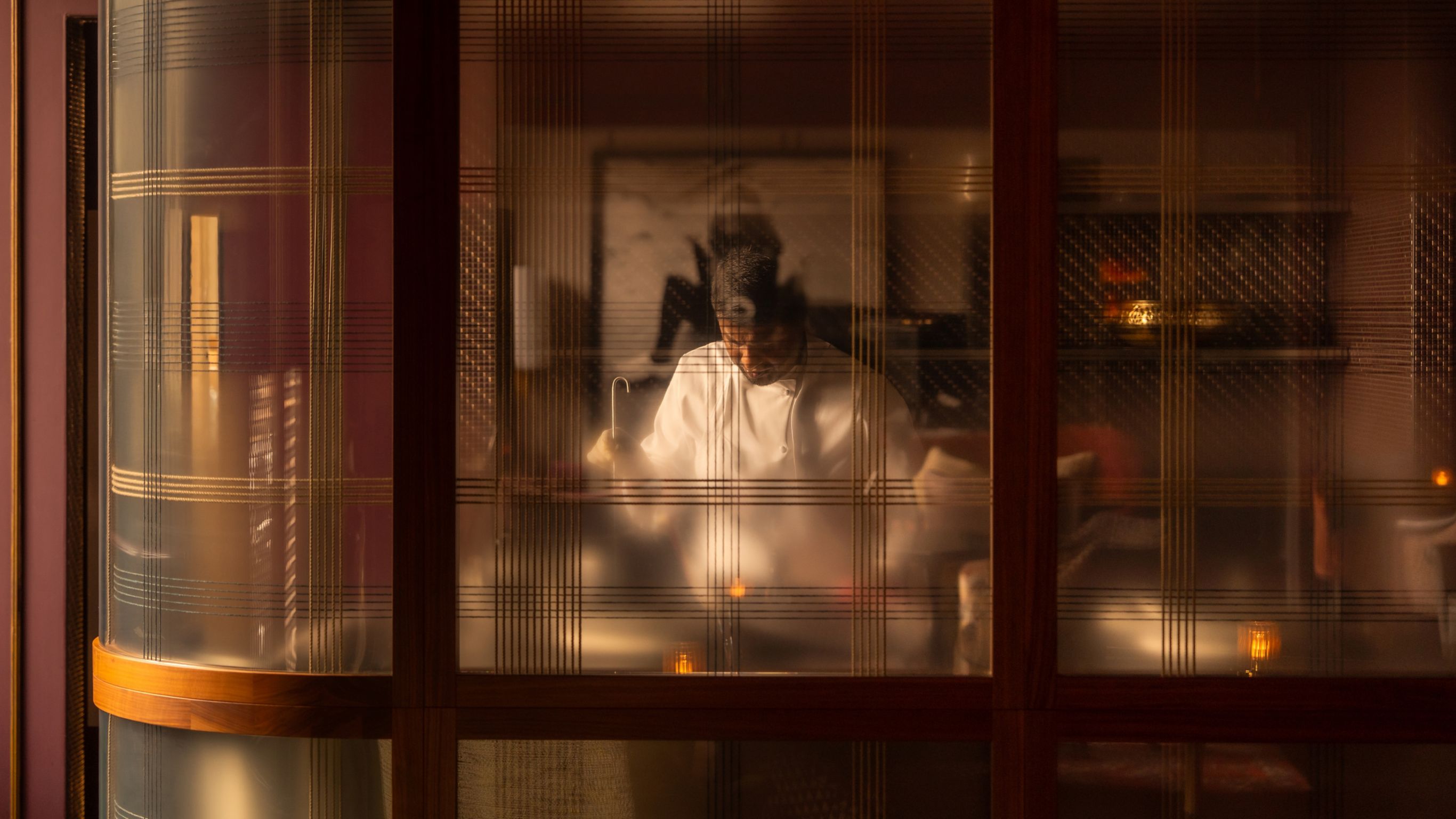 Blurred view of a chef in a kitchen through a  patterned glass door.