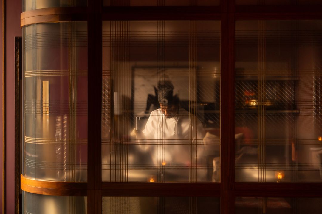 Blurred view of a chef in a kitchen through a  patterned glass door.