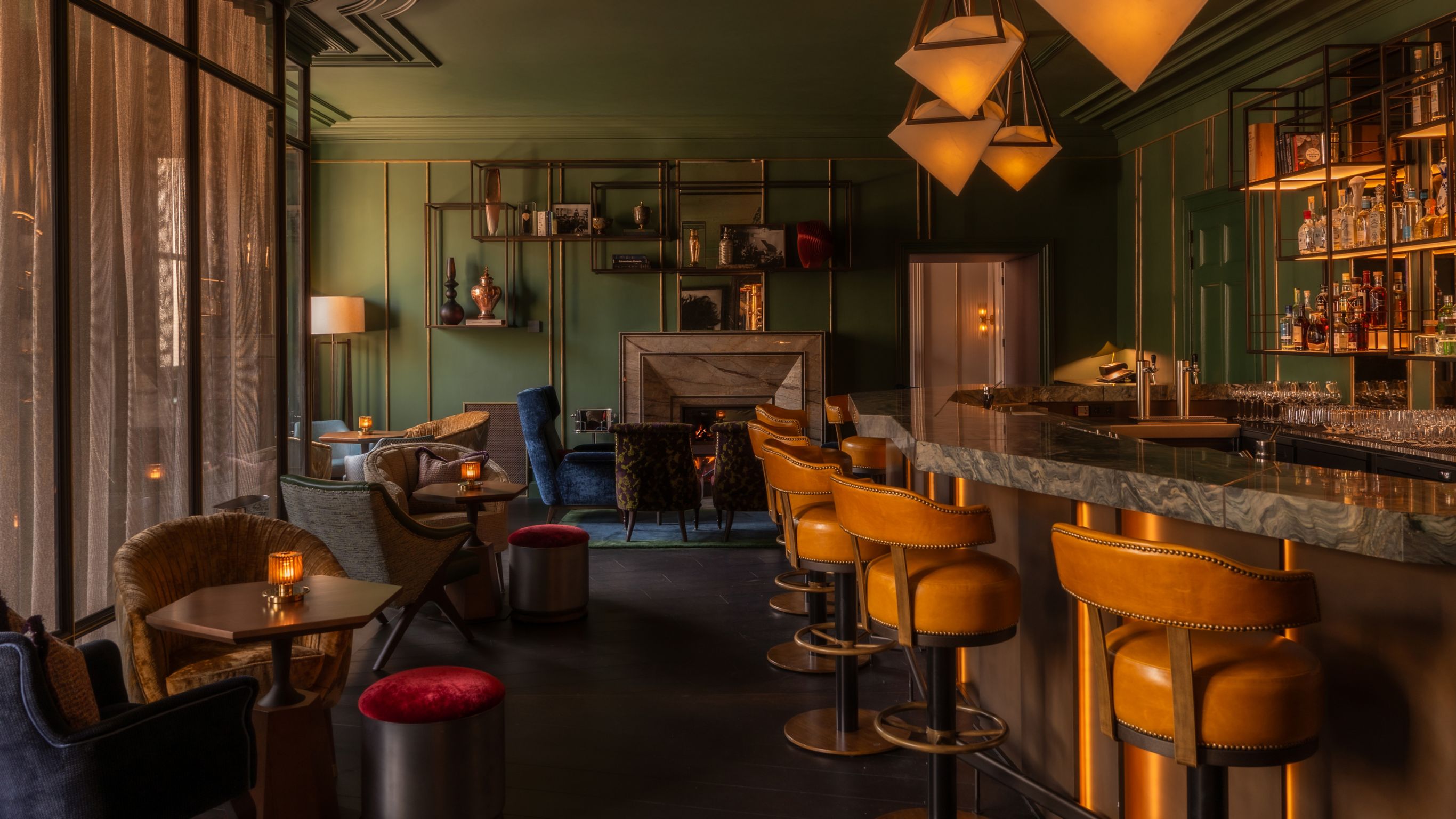 An Amsterdam bar with green walls, leather bar stools, and shelves displaying various bottles.