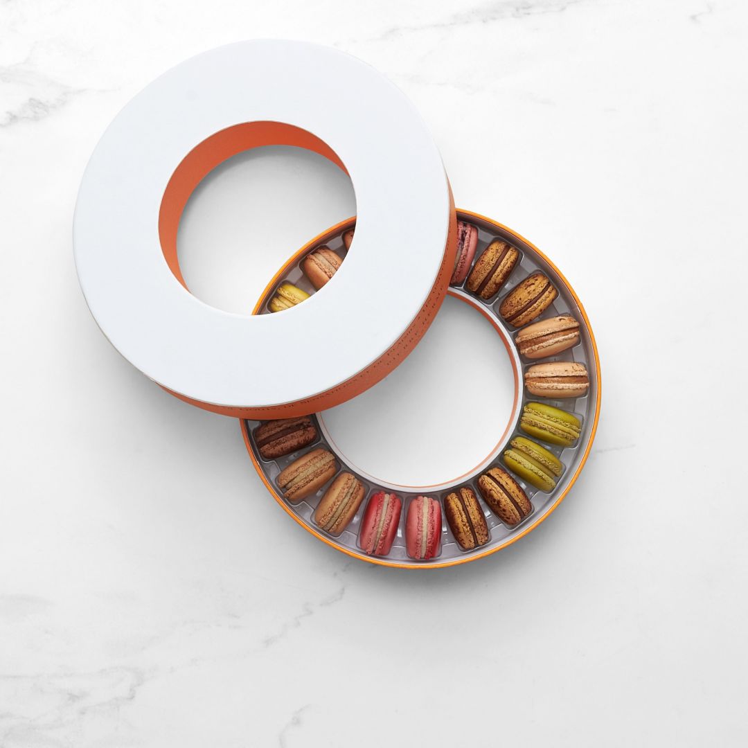 A circular box with an assortment of colorful macarons arranged in a circular pattern.