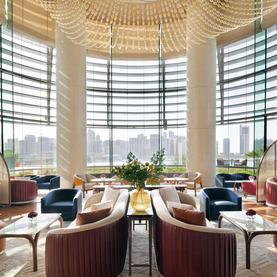 Lounge area with seating, tables, and decorative lighting featuring large windows with an Abu Dhabi view.