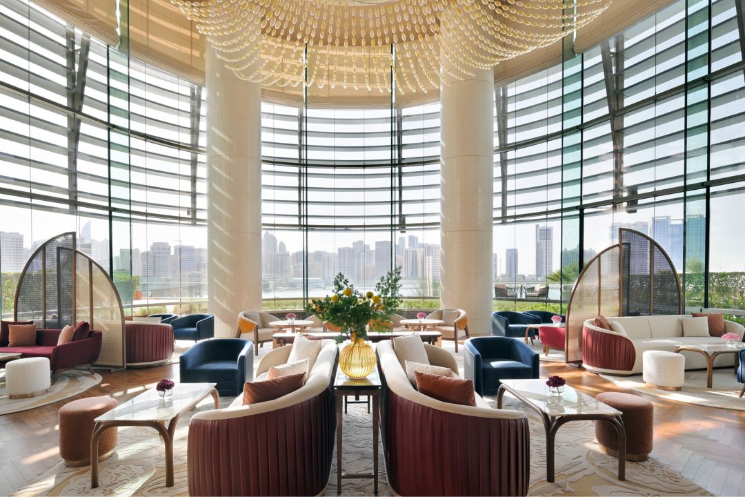 Lounge area with seating, tables, and decorative lighting featuring large windows with an Abu Dhabi view.