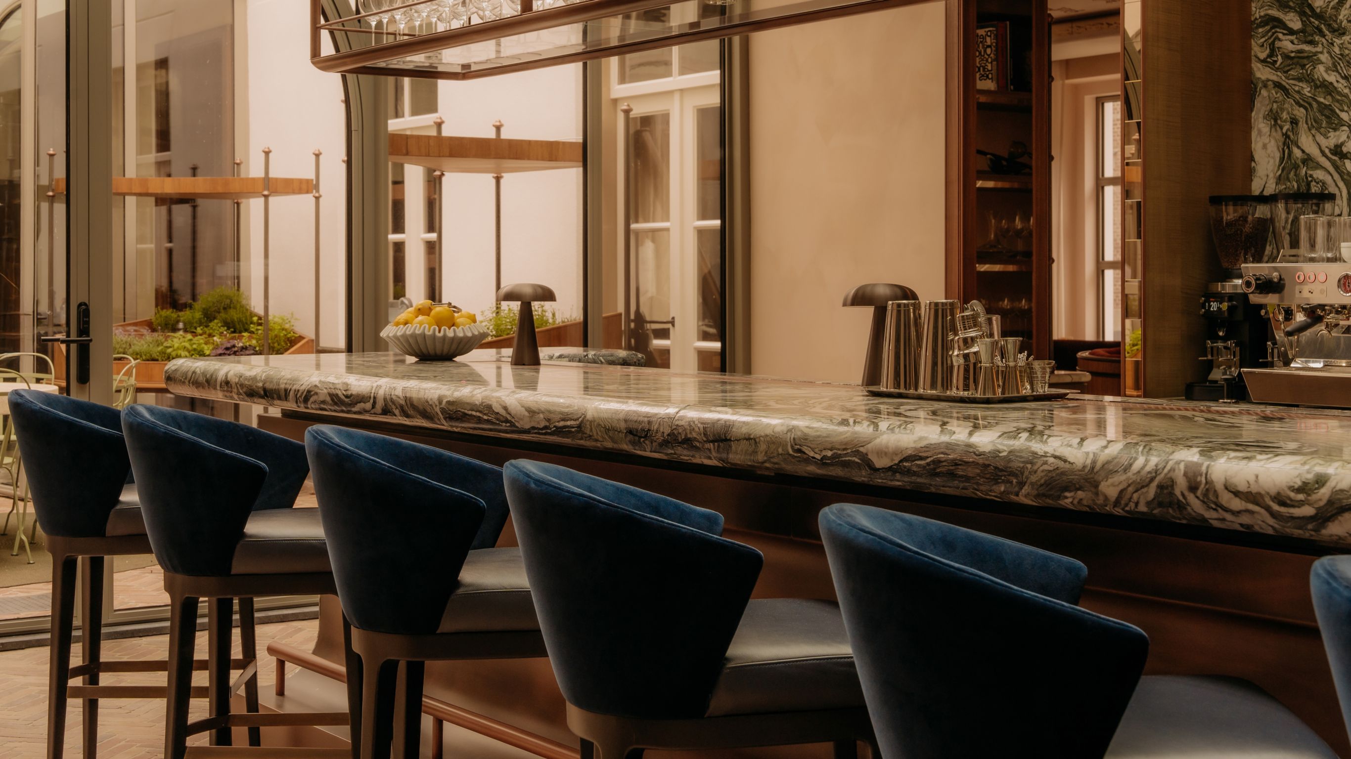 Bar counter with blue bar stools, a bowl of lemons, and a coffee machine in the background.