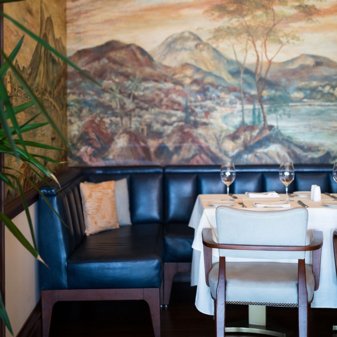 A corner booth at Island Brasserie in Bermuda, adorned with a white tablecloth and wine glasses, set beneath Pan Am Sky Club murals.