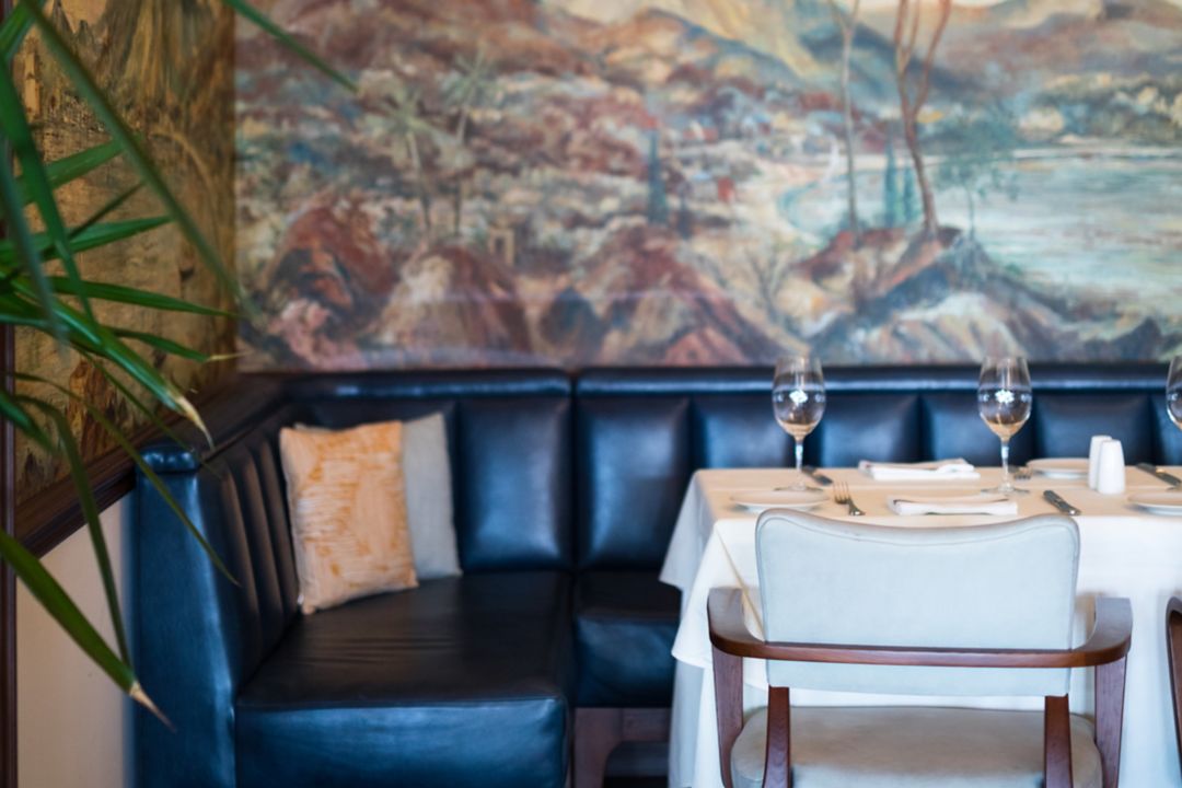 A corner booth at Island Brasserie in Bermuda, adorned with a white tablecloth and wine glasses, set beneath Pan Am Sky Club murals.