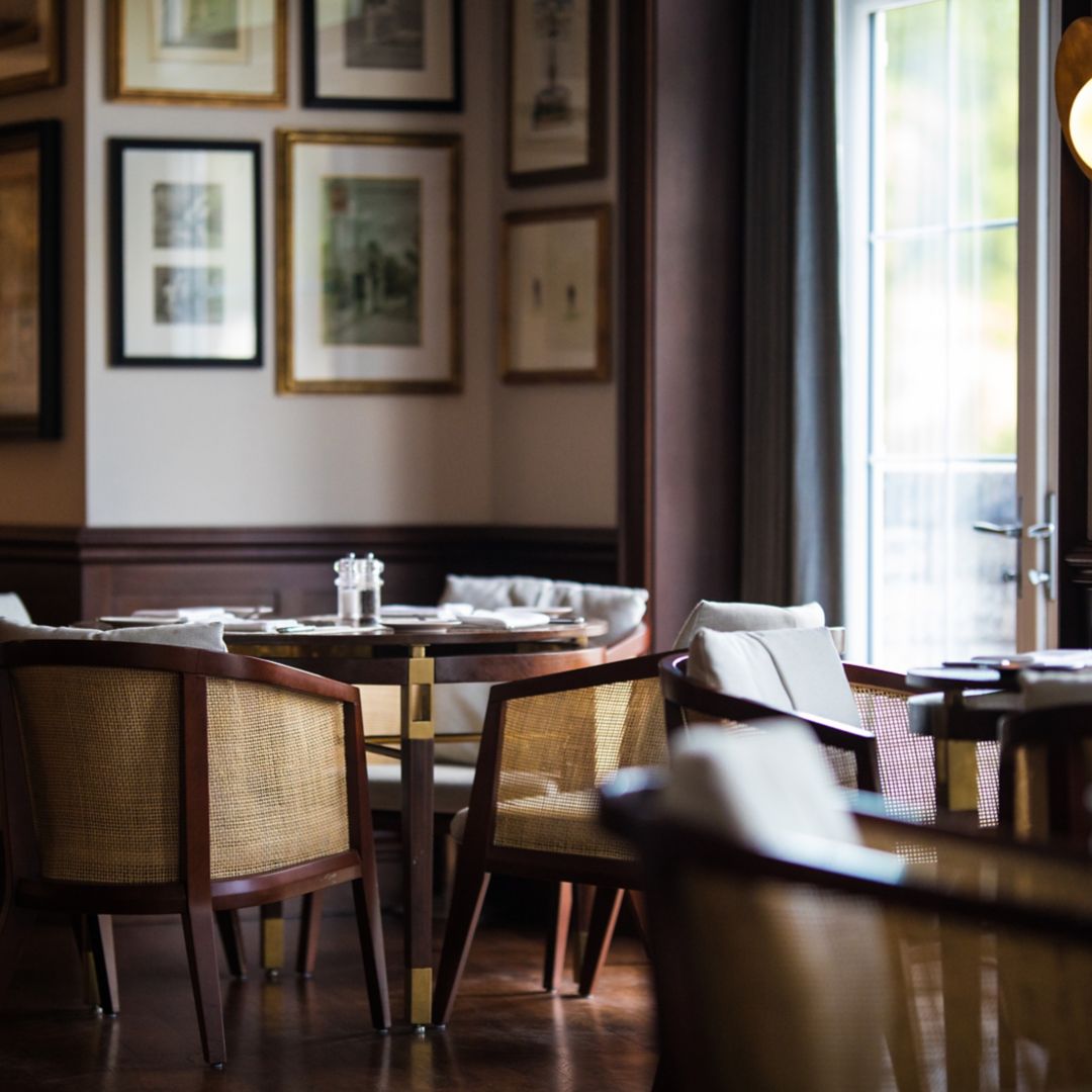 A wooden table with four chairs sits by a window at Tuckers Bar, with picture frames on the wall.