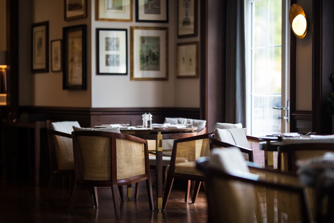 A wooden table with four chairs sits by a window at Tuckers Bar, with picture frames on the wall.