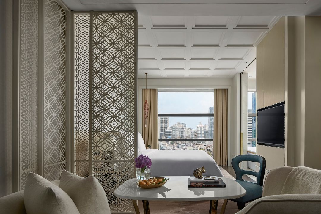 A hotel room with a decorative screen, modern furnishings, and the city view of Bangkok through large windows.