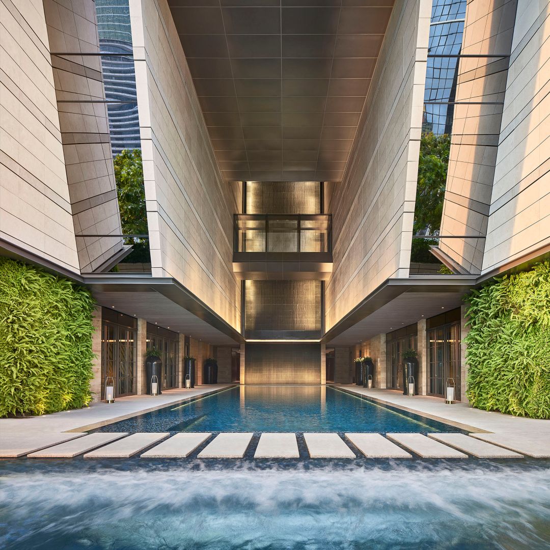 A hotel pool next to a luxurious lounge with multiple tables and plush seats and a view of the city.