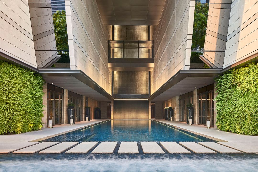 A hotel pool next to a luxurious lounge with multiple tables and plush seats and a view of the city.