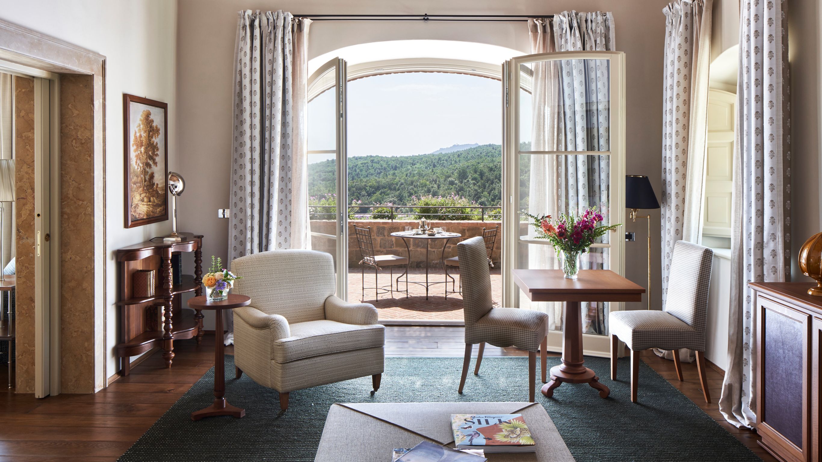 A luxury hotel room with open doors to a balcony overlooking a green landscape