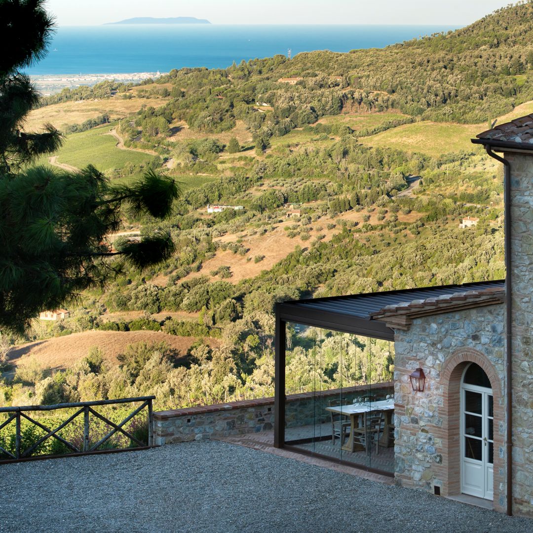 A building with an outdoor extension overlooking a hilly landscape with the sea in the distance.