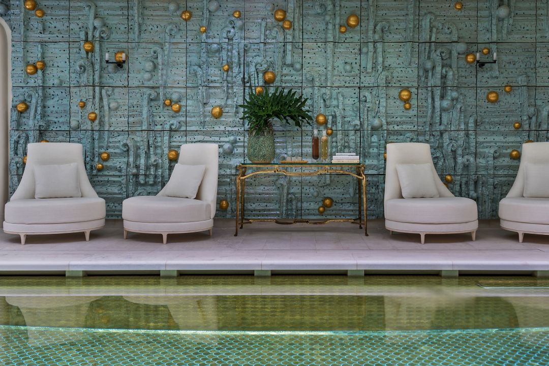 Four lounge chairs by an indoor pool and a decorative wall with gold accents.