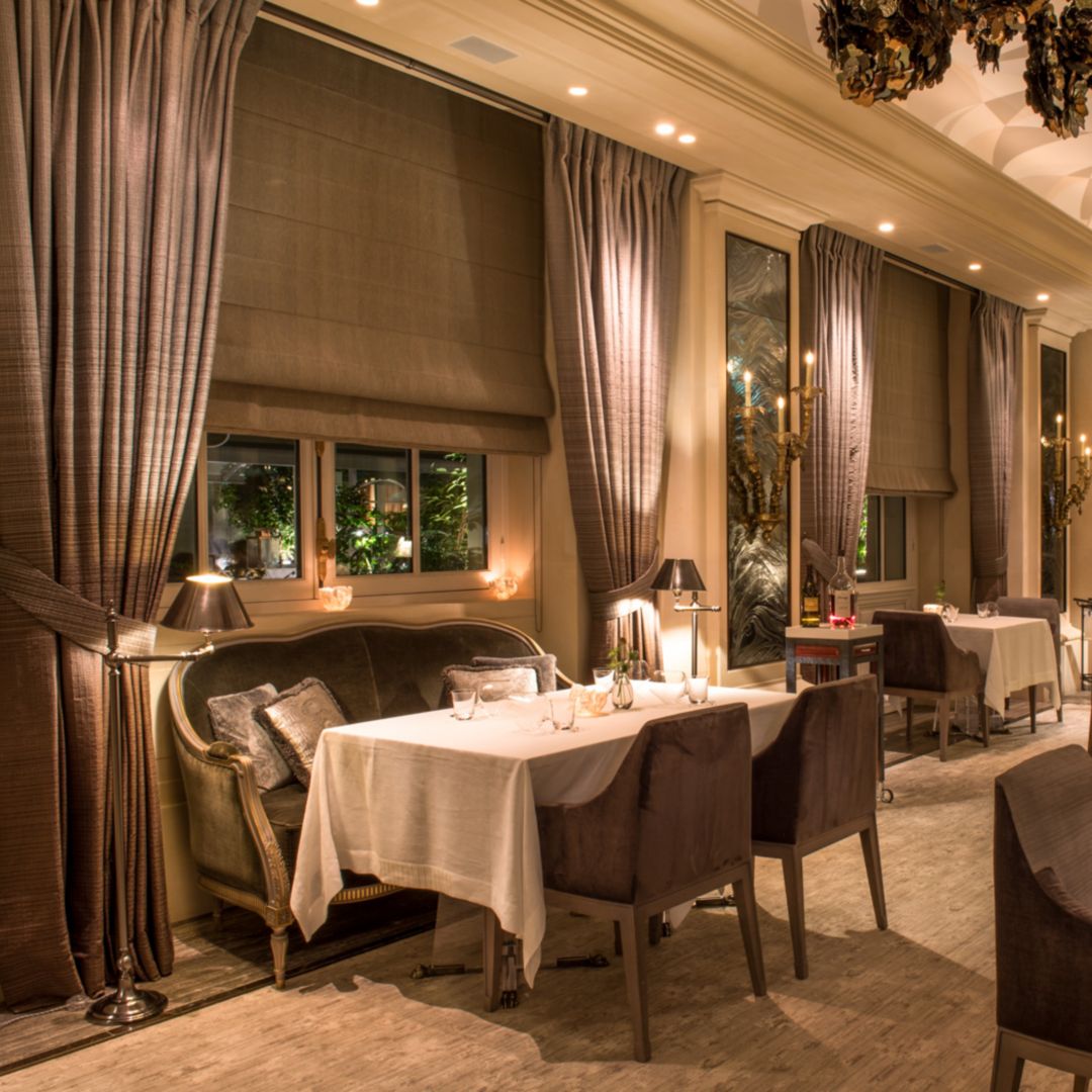 A restaurant with tables set for dinner, featuring plush chairs and draped curtains.