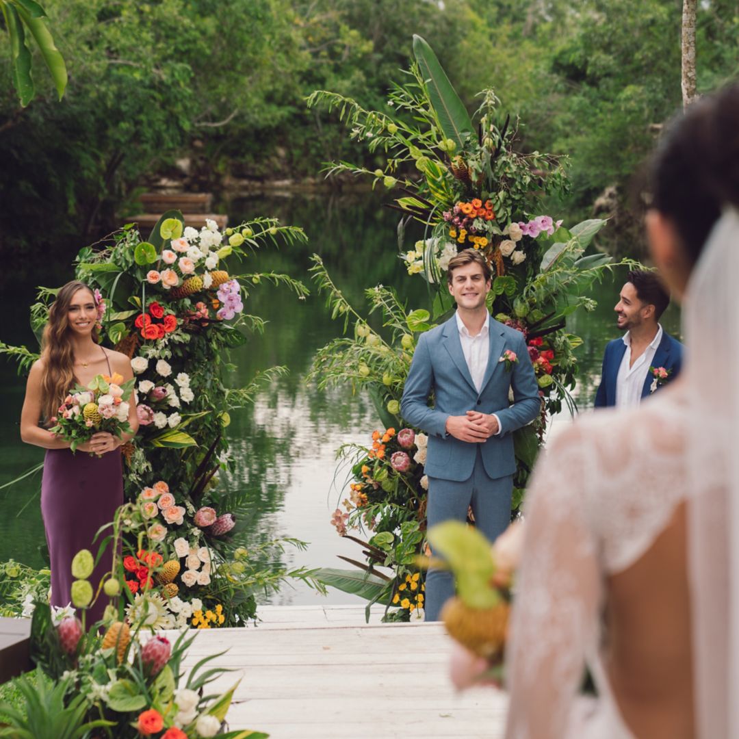 Bride sading in front of lagoon with large boquet of verdant green leaves and tropical flowers