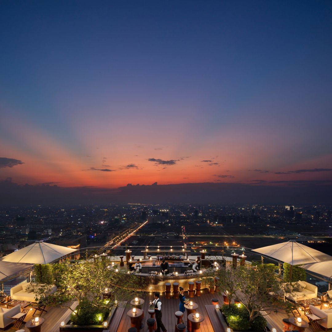 A rooftop bar in Phnom Penh at sunset with a view of the city skyline.