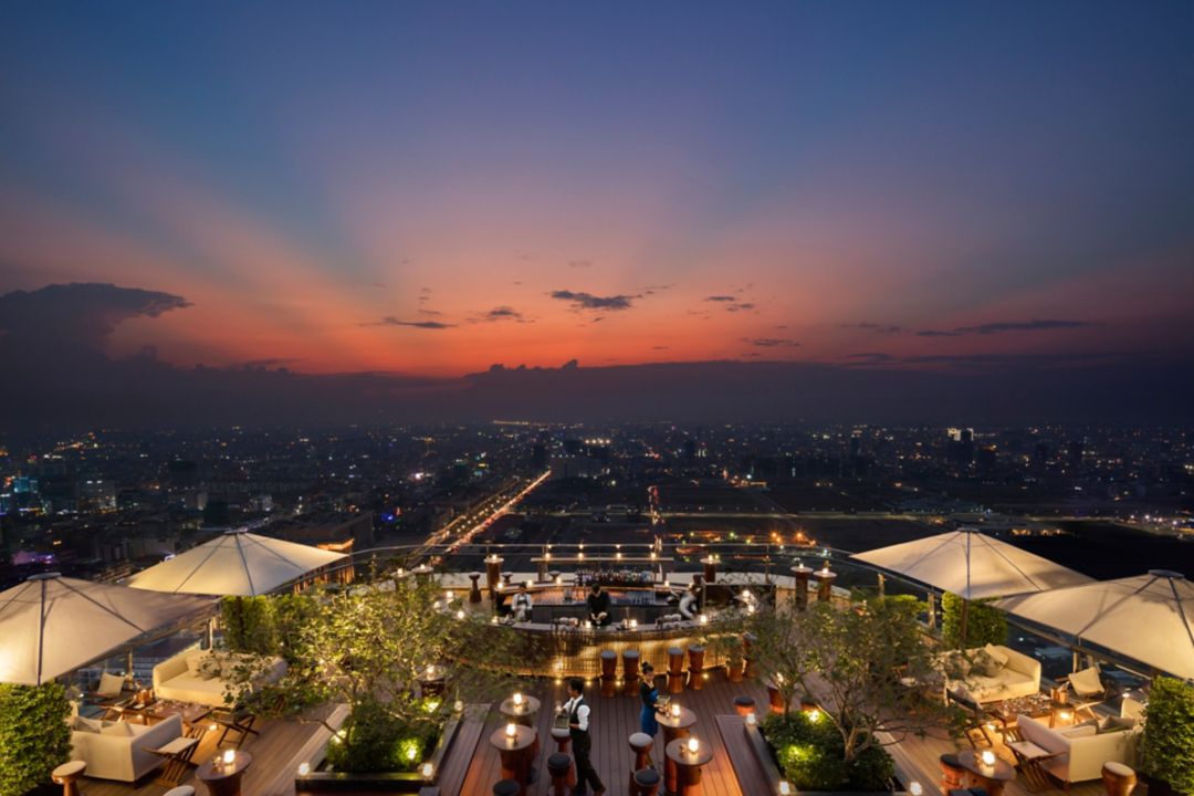 A rooftop bar in Phnom Penh at sunset with a view of the city skyline.