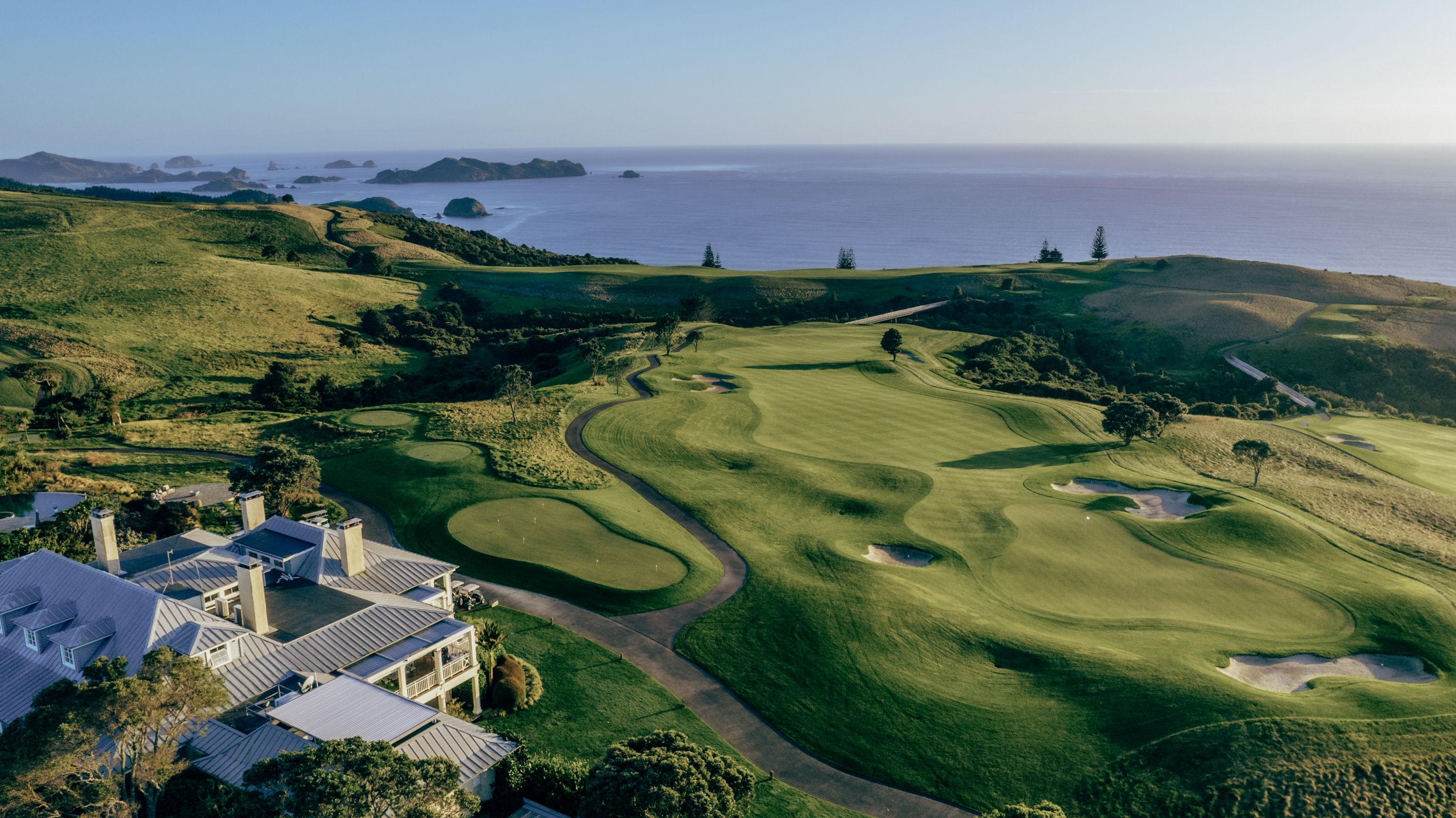 Aerial shot of Rosewood Kauri Cliffs main lodge overlooking the manicured golf course out to the Pacific Ocean with glimpses of the Cavalli Islands in the distance. 