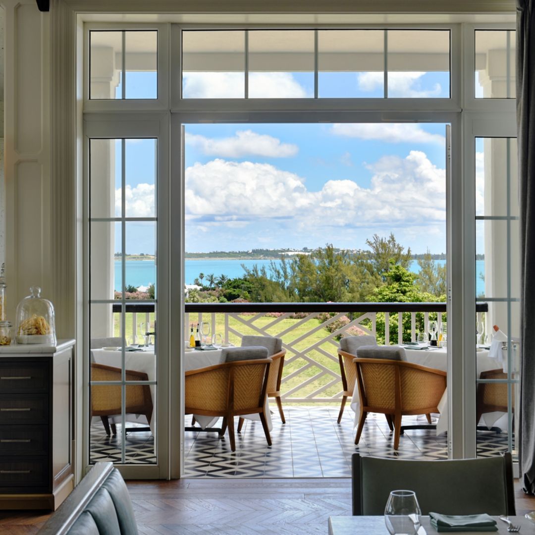 White doors lead to patio seating at Sul Verde restaurant, offering a scenic water view surrounded by lush greenery.