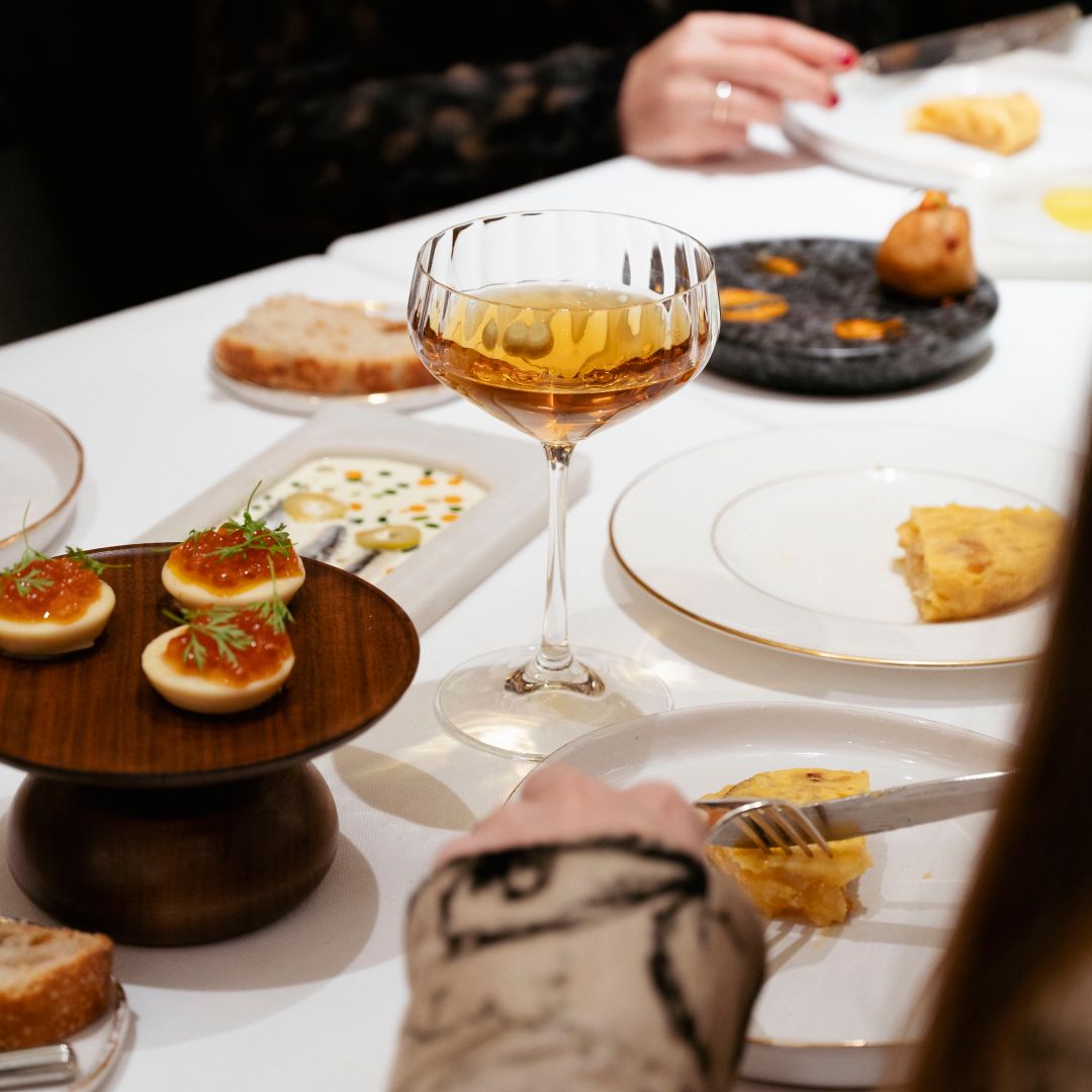 A table with small appetizers, bread, and shared plates of food, surrounded by people
