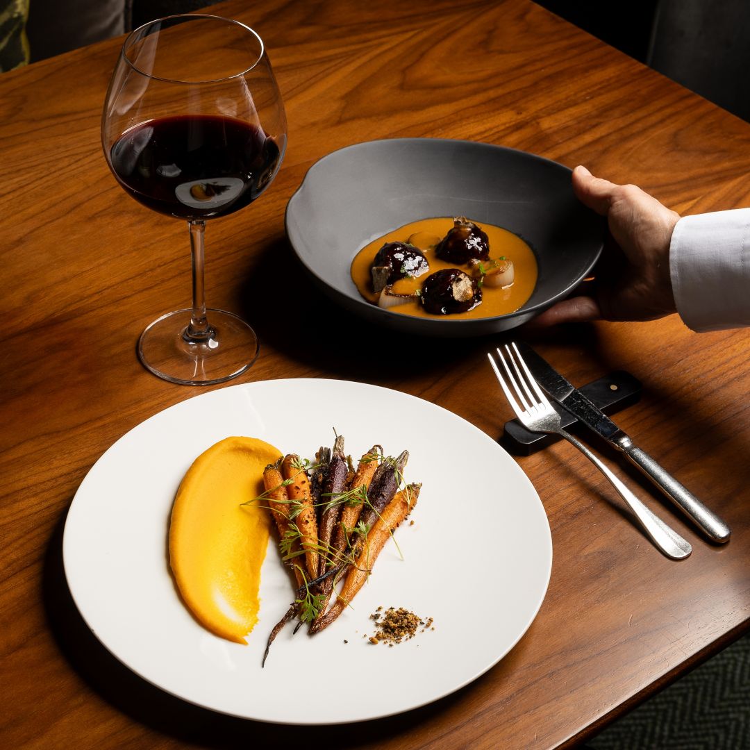 An outdoor dining area surrounded by greenery featuring tables set with dishes and comfortable seating.
